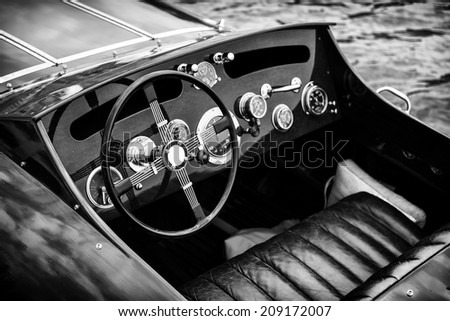 A view of the steering wheel and dashboard of an antique vintage wooden motor boat in black and white.