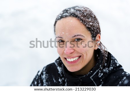 A portrait of a woman smiling outside in the winter with snow on her hair and face.
