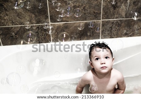 A small boy studies the bubbles floating down as he enjoys a bath.  Filtered for an vintage retro look.  Room for copy space.