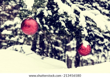 Two red Christmas ball decorations hanging off a spruce tree outside partially covered in snow.  Room for copy space.   Filtered for a retro vintage look.