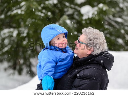A close up portrait of a smiling grandmother looking at her happy grandson while holding him outside while its snowing during the winter season