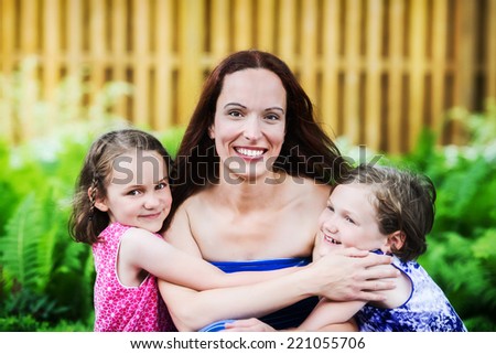 A close up family picture of two daughters on either side of their mother giving her a hug.