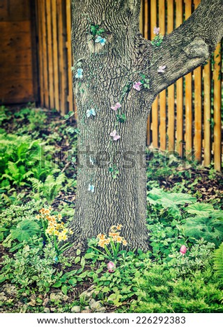 A back yard set up for an Easter egg hunt with hidden eggs and butterfly decorations on a tree.  Filtered for a retro vintage look.