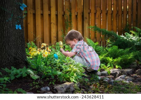 A little boy crouched down looking for Easter eggs in a garden on an Easter egg hunt during the spring season.