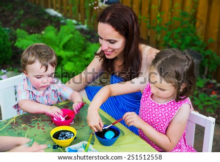 Family of children painting and decorating eggs outside during Easter in the spring season in a garden setting. . Mother smiles at her boy as he color dyes an egg pink.   Part of a series.
