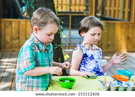 Children painting and decorating eggs.  A boy puts his egg in green dye at a crafts table outside during Easter in the spring season in a beautiful garden setting.  Part of a series.
