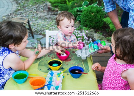 Family of children painting and decorating eggs outside during the springtime in a garden setting.  Father collects their finished color dyed Easter eggs in a carton.  Part of a series.