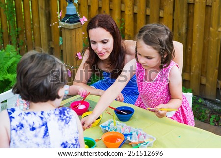 Family with children together painting and decorating eggs outside during the spring season in a garden setting.  Happy mother looks on as her kids color dye their Easter eggs.  Part of a series.