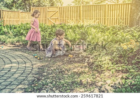 A girl with an Easter Basket collects colorful eggs as her sister comes to join the fun outside during an egg hunt.  Part of a series.  Filtered for a retro, vintage look.