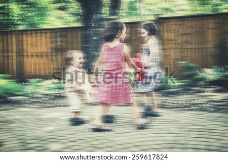 Children holding hands playing circle games with colorful plush bunny rabbits outside in a garden during an Easter party.  Intentional motion blur effect.  Filtered for a retro, vintage look.