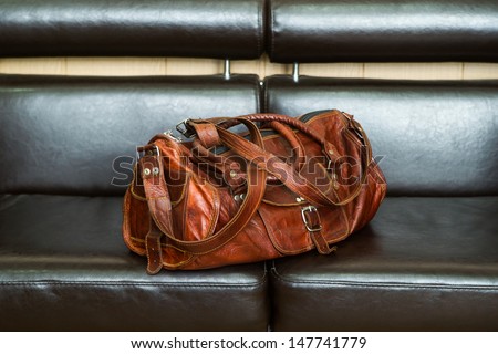 Luxury travel leather bag on black leather sofa