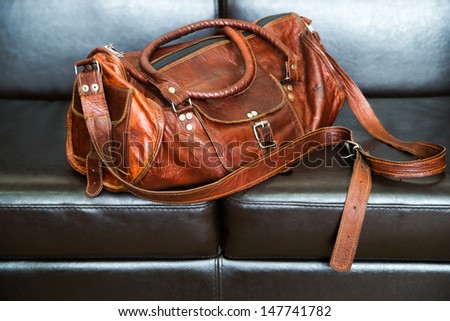 Luxury travel leather bag on black leather sofa