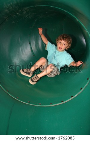 A little boy slides around the bend in a big green tube tunnel slide.
