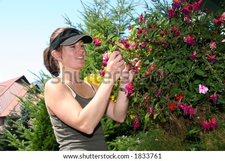 A woman landscape gardener smiles as she prunes a hanging basket full of flowers.