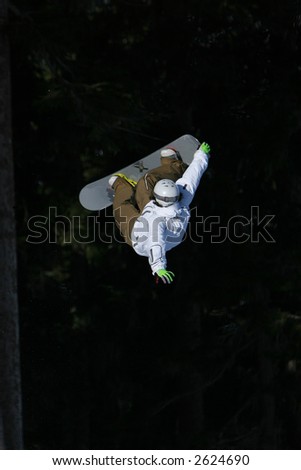 A snowboarder in bright clothes does an extreme air in front of a dark background.