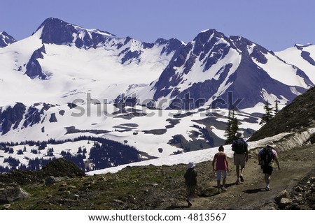 A family hikes in an alpine meadow with snow capped mountains during summer.