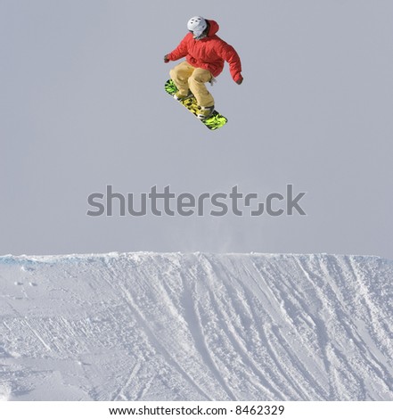 A snowboarder in bright clothing jumps in the crisp mountain air on cloudy day.