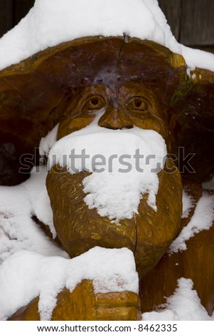 A chainsaw carving covered in snow stands guard outside a log cabin.