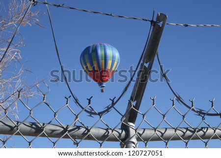 A hot air balloon in the Albuquerque Balloon Festival, seen through a barbed wire and chain link fence, showing they are prevented from landing and limiting freedom of flight - horizontal orientation