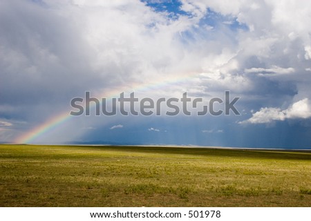 A half-rainbow reaches into the clouds at the edge of a storm over the plains of northern New Mexico