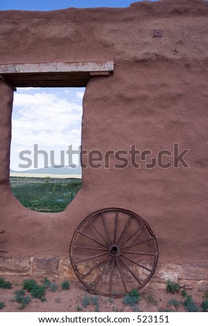 Adobe walls and window gaps form part of the stables and mechanics' work area, with wagon wheel, at old Fort Union National Monument north of Santa Fe, New Mexico