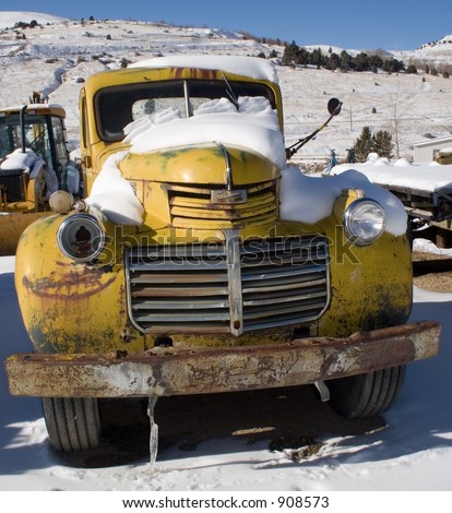 Old yellow truck in the snow, with mountain behind