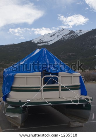A pontoon boat, stored in the mountains of Colorado, covered with a blue plastic tarp for the winter.