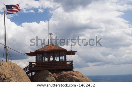 A fire lookout watchtower, flanked by the American flag, on top of the Devil\'s Head rock formation in central Colorado - horizontal orientation