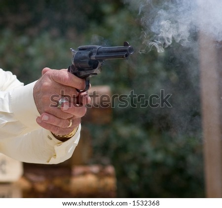 Smoke and flame come from the barrel of a pistol fired in the hands of a quickdraw artist in competition