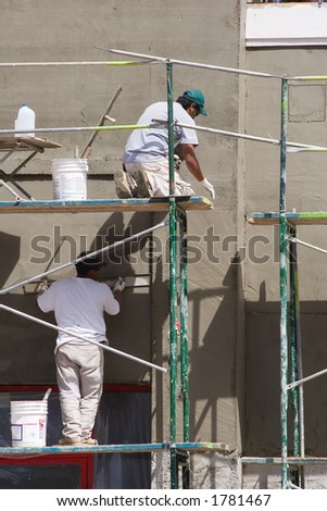 Two construction workers smooth the stucco wall on a new building