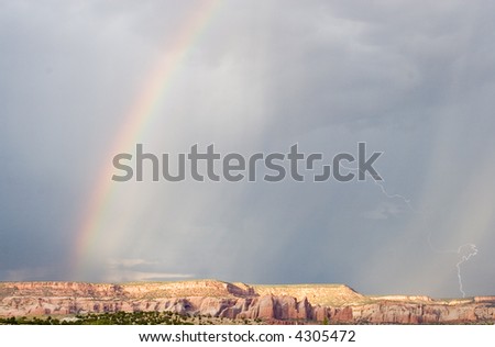 Rain, a rainbow and lightning, simultaneously captured over a red rock mesa in northwestern New Mexico