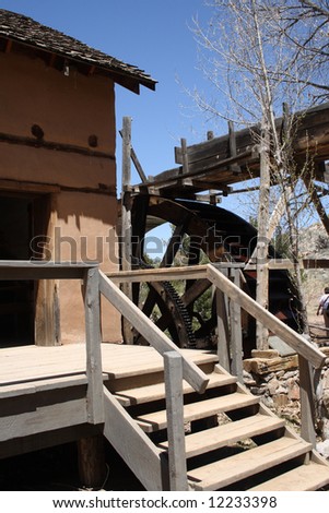 A old, but fully-working water-driven mill, with a rather large wooden waterwheel, located on the grounds of a museum in New Mexico, complete with adobe walls