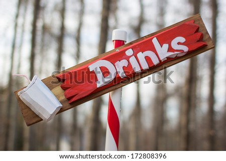 Handmade red and white wooden sign with Drinks painted on the sign.  Mounted on a candy stripe pole.  Shallow depth of field.