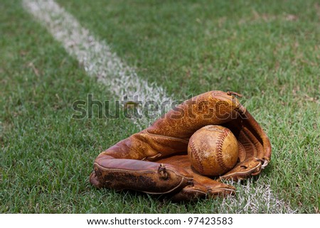 Old baseball and baseball glove lying on the foul line on a baseball field.