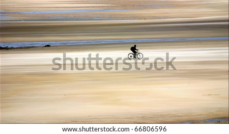 Bike rider alone on wide flat beach at low tide near Bamburgh in Northumberland.
