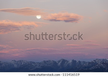 Sunset over the mountain peaks with full moon