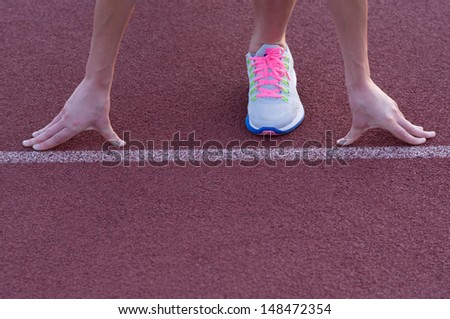 Athletic teenage girl in start position on track .