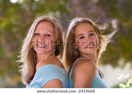 stock photo Two pretty blond teen girls sitting backtoback with wind