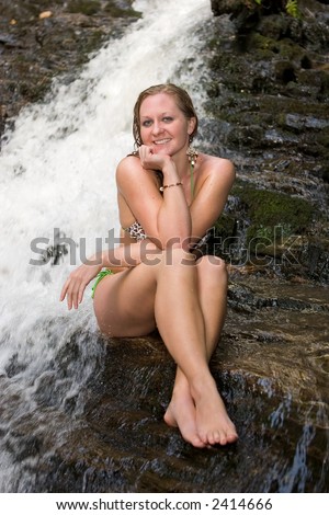 Wet girl in bikini on rocks with legs crossed and elbows on knees at Mingo Falls, Cherokee, NC.