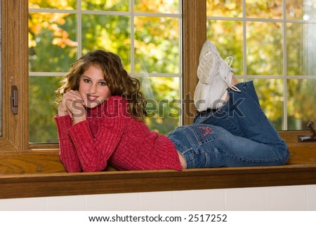 Happy and spirited portrait of a 12 year old girl on her belly in a window sill.