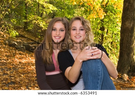 18 year old big sister beside 13 year old little sister outdoors under trees in early fall.