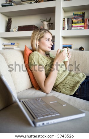 A young woman on the sofa with her laptop and a mug of coffee