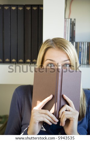 A young woman peeping from behind her book