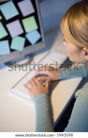 A young woman at her computer with post-its on the monitor