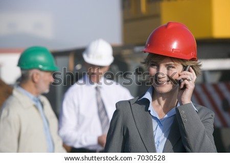 A woman construction engineer on the phone with co-workers behind her