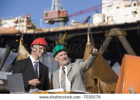 Two oil platform inspectors with a laptop, with the platform in the background