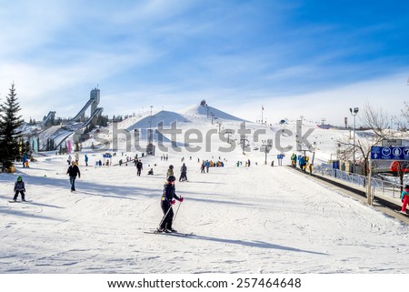 CALGARY, CANADA - MAR 1: People enjoying the skiing at  Canada Olympic Park on March 1, 2015 in Calgary, Alberta.  Visible are skiers at the base of the hill. Ski jump towers are on the top left.