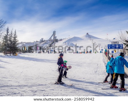 CALGARY, CANADA - MAR 1: People enjoying the skiing at  Canada Olympic Park on March 1, 2015 in Calgary, Alberta.  Visible are skiers at the base of the hill. Ski jump towers are on the top left.