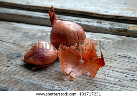Black onions on an old rustic wooden background, with one peeled onion skin