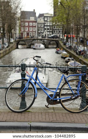 blue bike on canal, amsterdam old bike parked at a bridge railing, in background canal with tourist canal boats in city center